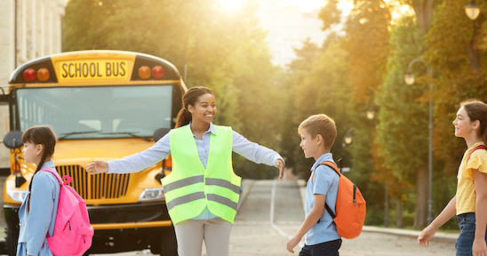 Kids crossing the street with a crossing guard. 